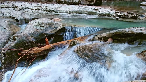 Mountain river with crystal-clear water, small cascade of turquoise water, and log lying across river, creating natural barrier. Slow motion. Not AI