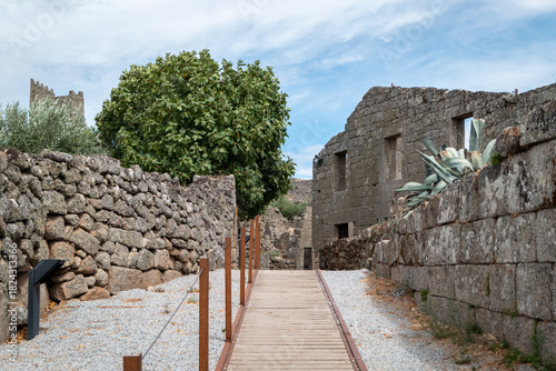 Caminho de acesso modernizado entre muros de pedra, ruínas e vegetação, há aldeia histórica e muralhada de Marialva em Portugal