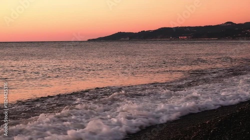 Magnificent, dramatic sunset over sea, the ocean, shimmering golden waves crashing against rocky, stone shore. Quiet night. Nature, background, travel, relaxation. No people. Slow motion. Not AI