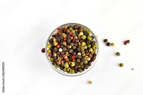 Different colored peppercorns in and around a glass bowl.
