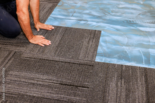 Skilled worker lays gray carpet tiles in an office area to create stylish functional workspace © ungvar
