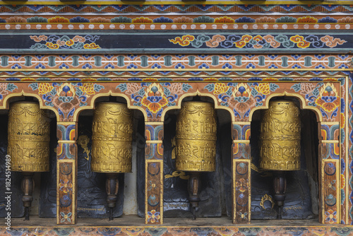 Gangtey Monastery, Bhutan - 20 September 2025: View of golden prayer wheels glimmering against the dark stone, framed by intricate, colorful carvings.