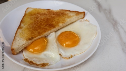 close up of a toast bread and two fried sunny side up eggs for breakfast on a white plate with copy space