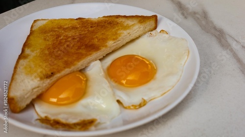 close up of a toast bread and two fried sunny side up eggs for breakfast on a white plate with copy space