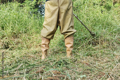 A man stands cutting grass on a clear day.
