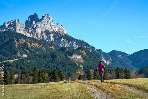 nice and active senior woman, riding her e-mountain bike in the Tannheim valley , Tirol, Austria, with  famous summits Gimpel and Rote Flueh