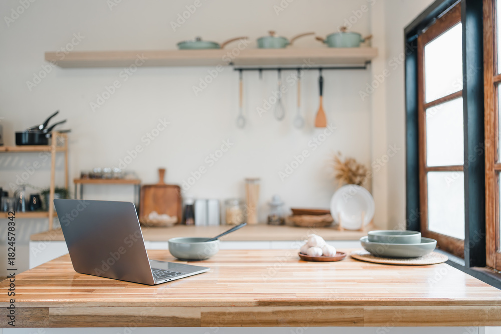 Obraz premium Modern laptop on wooden kitchen island with bowls, plate and utensils evoking cozy productivity and home cooking