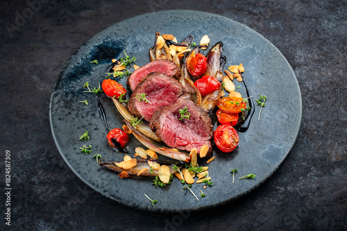Fine dry aged beef filet steak rare tataki style cut tagliata with caramelized chicorée, tomato and almonds served as close-up on a design plate