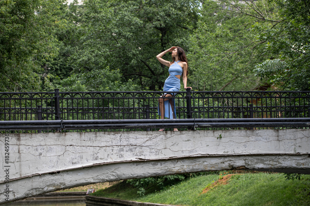 Naklejka premium Young beautiful brunette woman in blue knitted dress posing in summer park