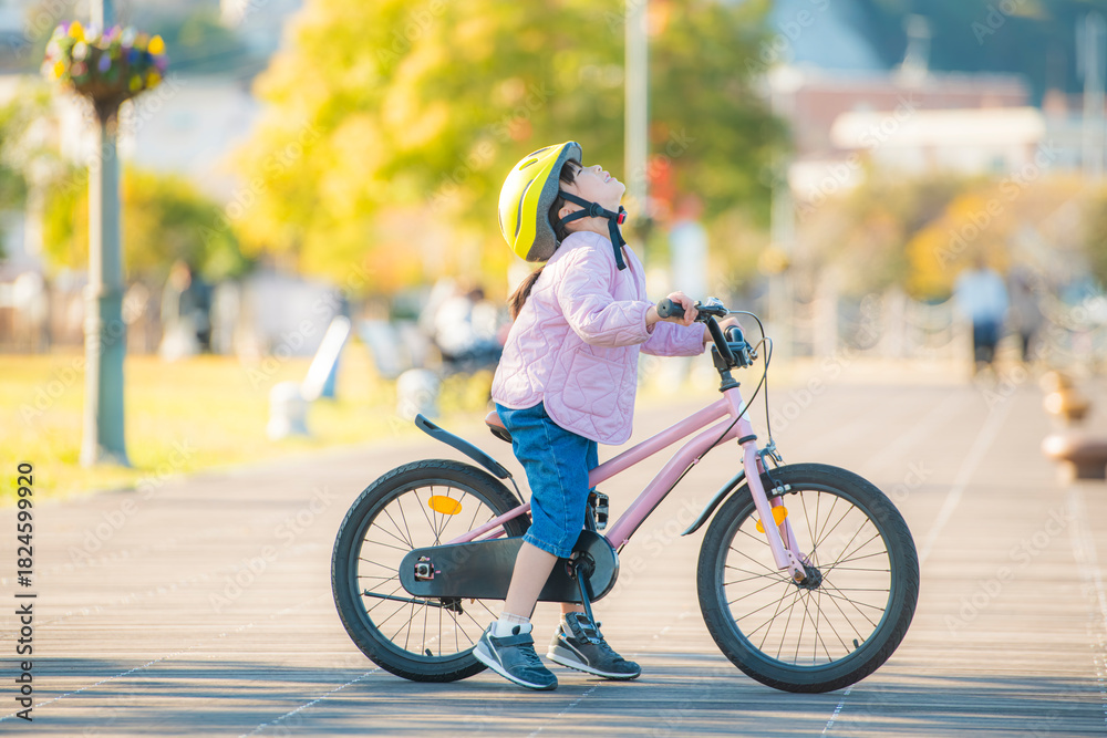 Obraz premium 自転車にまたがり空を見上げる女の子と明るい公園の屋外風景
