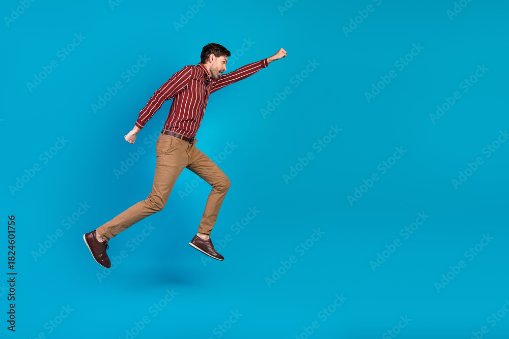 Obraz premium Young handsome man in casual shirt and tan pants leaps in mid air against blue background