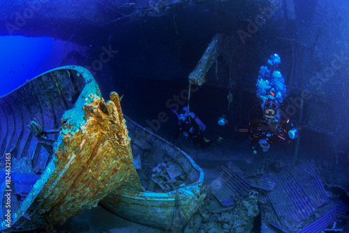 Scuba divers explore the deep wreck of the Salem Express, illuminated by blue ambient light and surrounded by corroded metal structures on the seafloor.