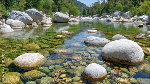 Clear shallow river water flows over smooth riverbed stones and boulders.