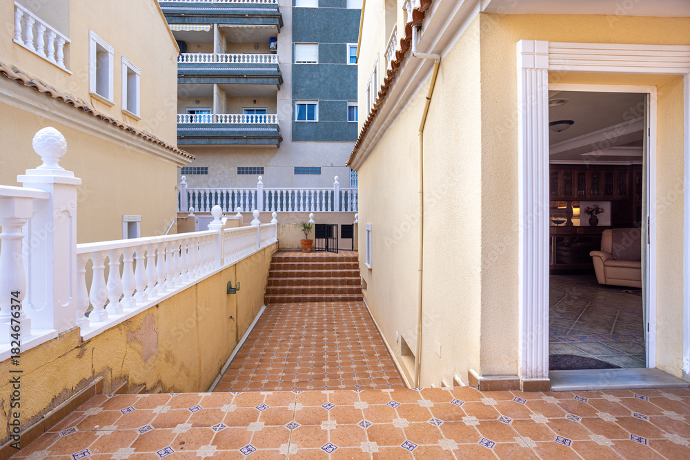 Obraz premium Sunny Mediterranean patio with tiled flooring, white balustrade, and stairs to residential entrance