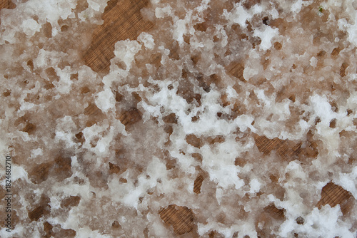 Melting, slushy snow reveals the striking wood texture beneath. The strong contrast between white and brown captures the vivid moment of thaw beautifully.