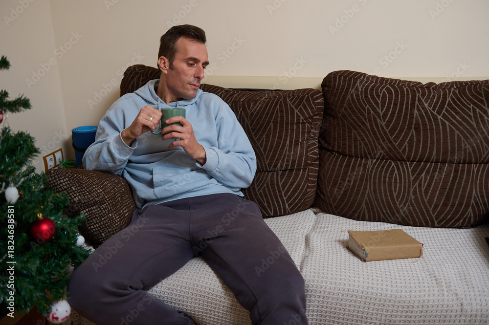 Fototapeta premium Relaxed Father Working From Home On Couch With Coffee Near Christmas Tree