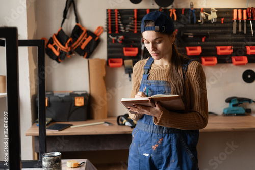 Job occupation concept. young female worker in uniform holding notepad in her carpentry workshop.