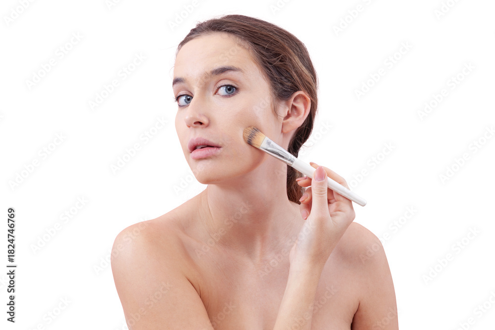 Fototapeta premium Young woman with natural skin applying foundation with a makeup brush, visible streak on cheek. Skincare and beauty routine concept. Isolated on white background, clean and minimal look