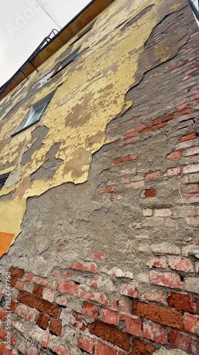 Old decaying building facade with peeling yellow paint and exposed brick wall, vintage urban texture, weathered exterior surface, damaged plaster and rough bricks