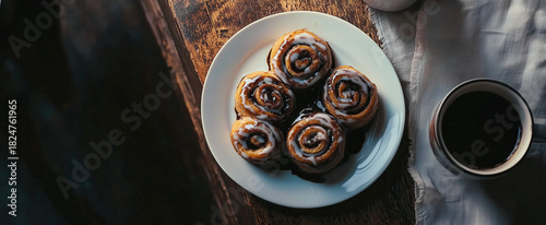Freshly baked cinnamon rolls with icing beside a steaming cup of coffee.