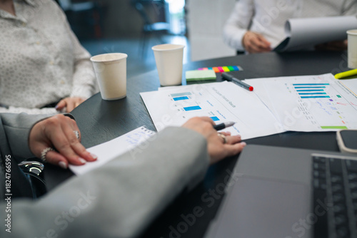 Businesspeople analyzing printed charts and bar graphs during meeting, close-up view of hands and documents
