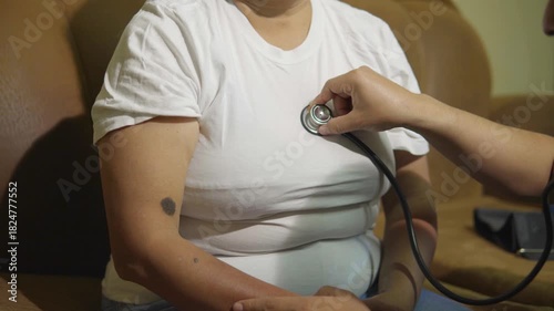 Unrecognizable nurse listening to the heart of a middle-aged female patient