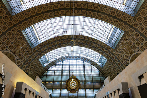 Low angle symmetric interior view of the main hall of the 1900 former Gare d’Orsay, now the d’Orsay Museum’s  glass roof and clock, Paris, France 