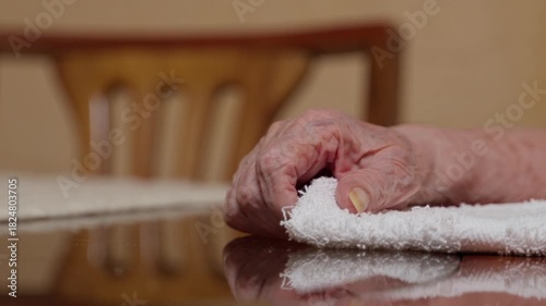Detailed close-up of an anonymous elderly woman’s hand gently touching a white towel on a polished table. The scene conveys age, reflection, and calm.