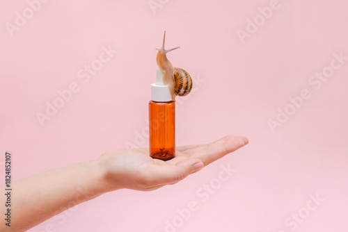 Glass cosmetic bottle with snail in hand. Mockup for your brand. Skin care product, spa, luxury, natural beauty