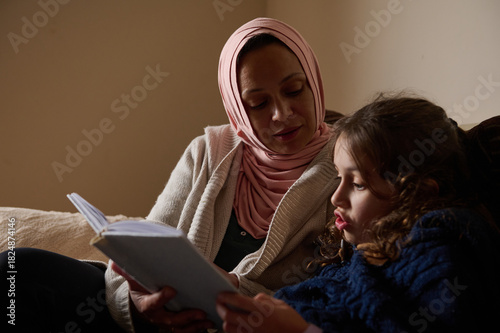 Mother And Daughter Reading Together At Home: Modern Muslim Woman In Hijab In Europe Lifestyle