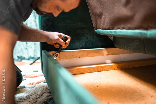 фотографія Man disassembling sofa furniture mechanism at home using furniture wrench