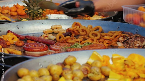 A vibrant array of street food is displayed in large metal trays, featuring crispy fried snacks, assorted sausages, and fresh fruits, creating an inviting culinary scene