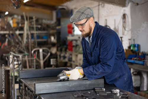 Experienced mechanic uses an angle grinder while working at a machine-building plant