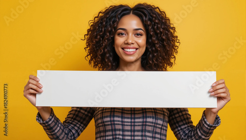 Smiling woman holding empty white poster on yellow background
