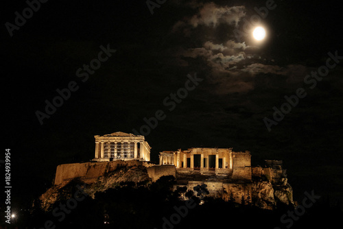 Schilderij op canvas Ancient greek acropolis illuminated at night under a full moon and cloudy sky