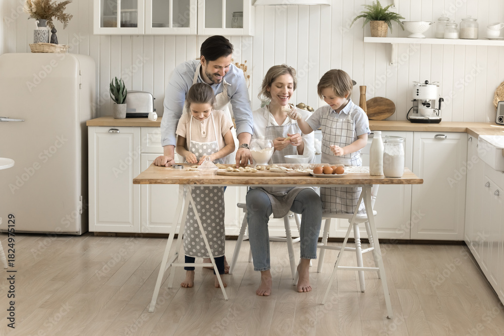 Obraz premium Couple with two diverse young kids cook dumplings at kitchen