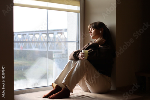Pensive woman enjoying a quiet moment by the window with a warm drink