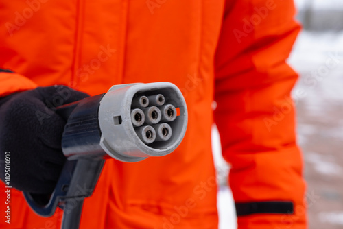 fast charging connector Close-up, electric car charging plug held man in orange jacket, connection point for DC electric vehicle refueling, EV technology, future mobility against charging station