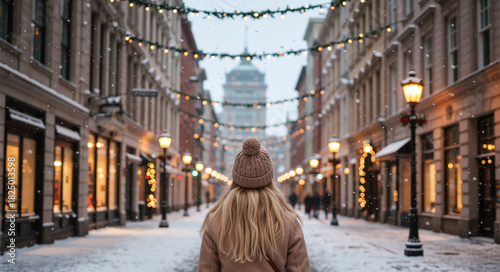 A woman seen from behind on a snowy city street decorated with festive Christmas lights. Winter holiday travel in a historic old town