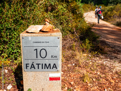 Trail marker showing 10 km to Fátima on Caminho do Tejo pilgrimage route, Portugal. Distance sign with pilgrims walking on scenic path with stacked stones