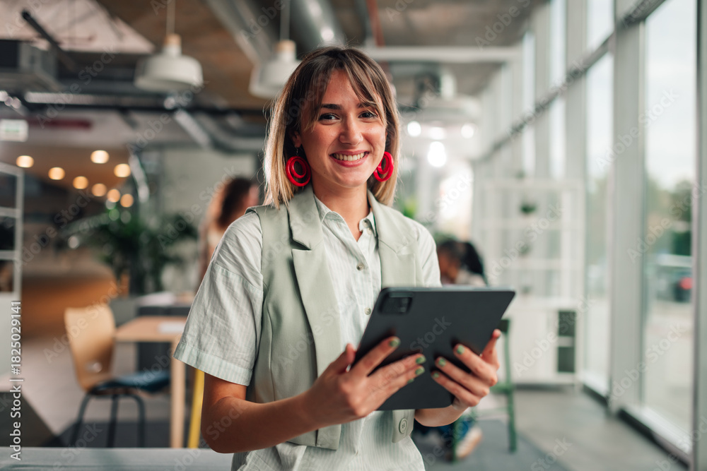 Fototapeta premium Young businesswoman smiling, holding tablet in modern office