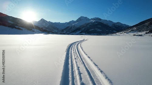 Cross-country ski tracks winding across a vast pristine snowfield towards sunlit mountains for a winter adventure concept and peaceful journey