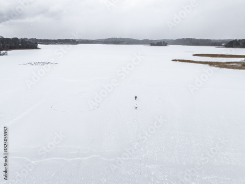 Aerial view of a solitary figure walking on the frozen Galvė Lake under a winter sky, the landscape a study in monochrome, Trakai, Trakai, Lithuania.