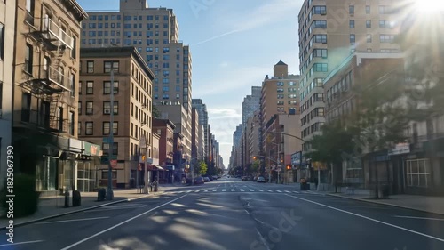 A straight, empty city street with tall buildings lining both sides, under a clear, bright sky