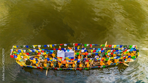 Aerial view of a vibrant boat adorned with colorful flags and people in yellow, gliding across the water, Buguma, Rivers State, Nigeria.