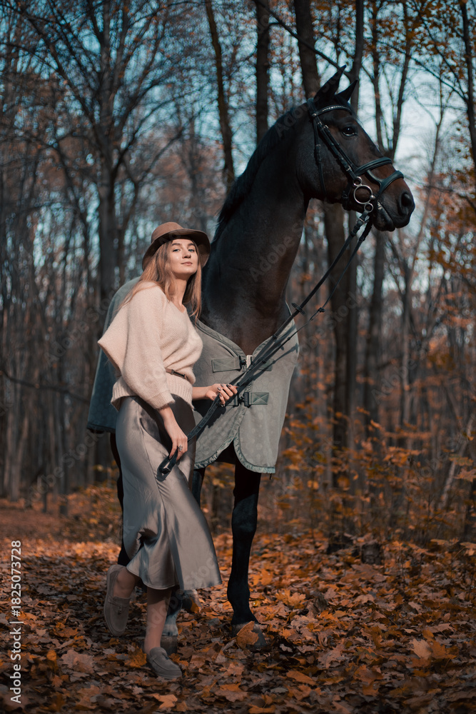 Naklejka premium Woman stands beside a horse in a forest with autumn leaves during daylight in October