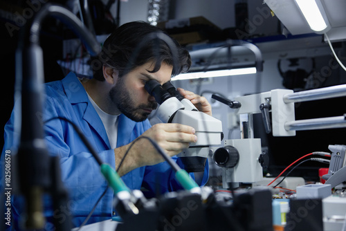 Technician working on circuit board under microscope in lab
