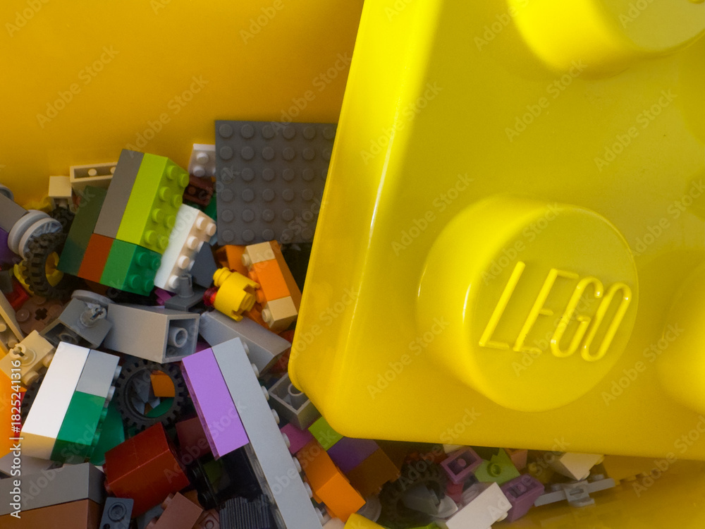 Fototapeta premium BELO HORIZONTE, MG, BRAZIL – NOVEMBER, 22, 2025: A close-up view of various colorful LEGO bricks spilled inside a bright yellow LEGO storage box.