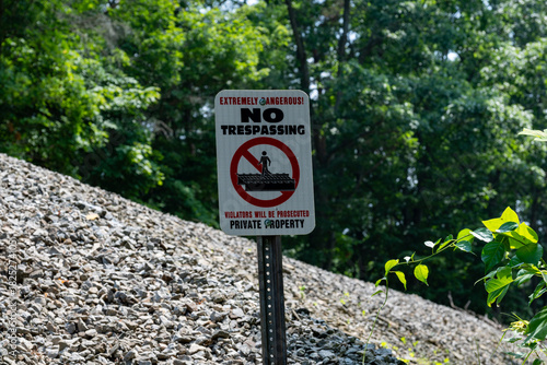 No trespassing sign warns of dangers on private property in wooded area during sunny day