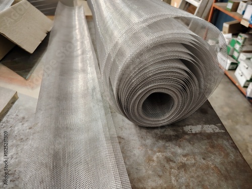 Shiny, flexible mesh rolled out on a metal surface, illustrating the typical material used for making windows and door fly screens.
